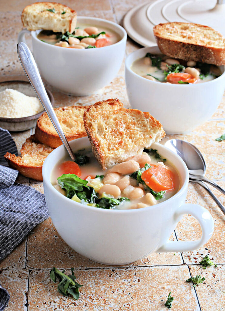 tuscan kale soup in white mug with toast and spoon on top