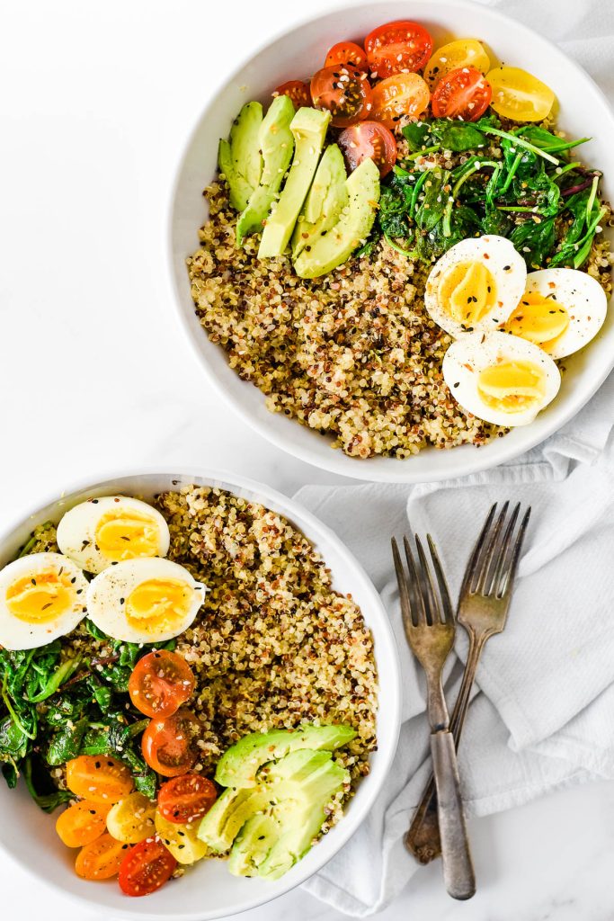 two white bowls with quinoa, veggies and hard boiled eggs