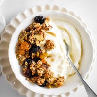 sourdough granola on yogurt in white bowl with spoon sticking out side