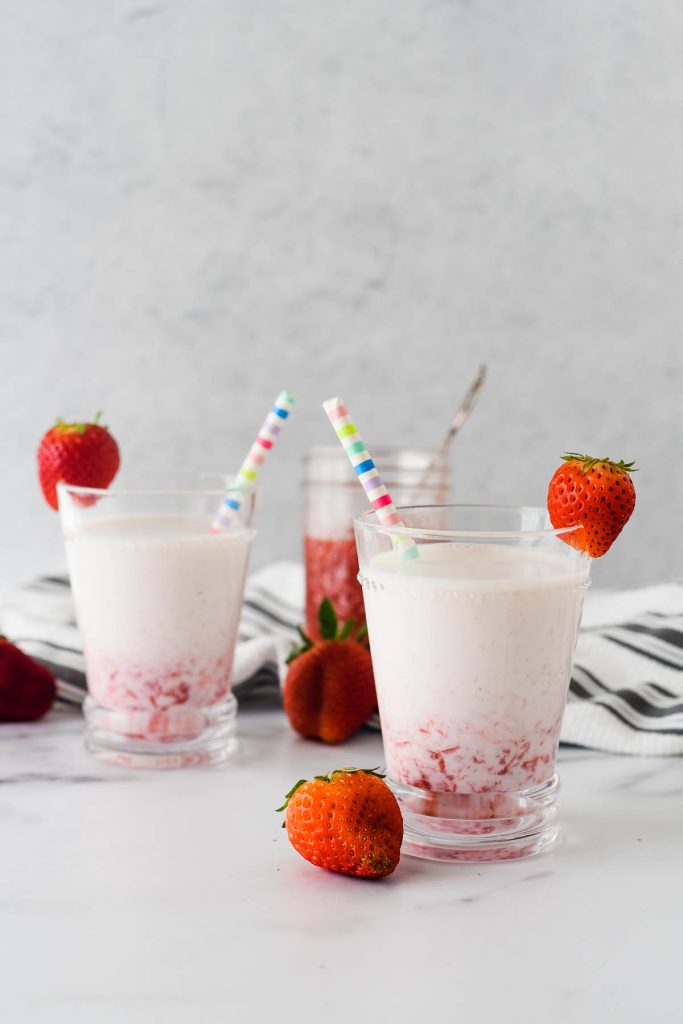 two glasses of homemade strawberry milk with berries beside
