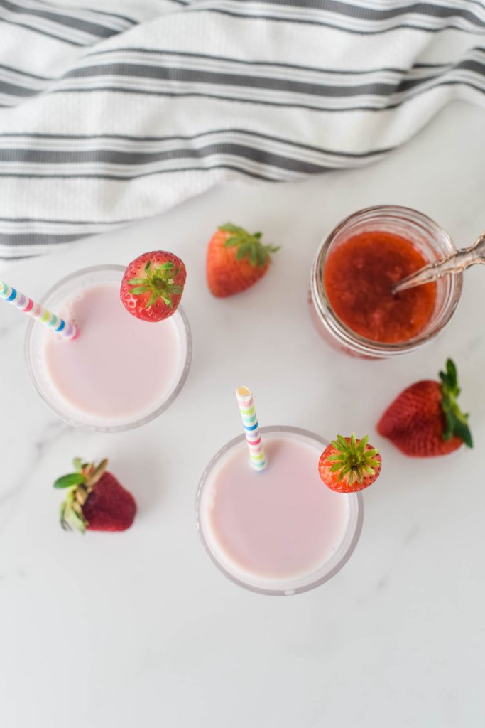 overhead image of two glasses with strawberry milk next to jar of strawberry puree
