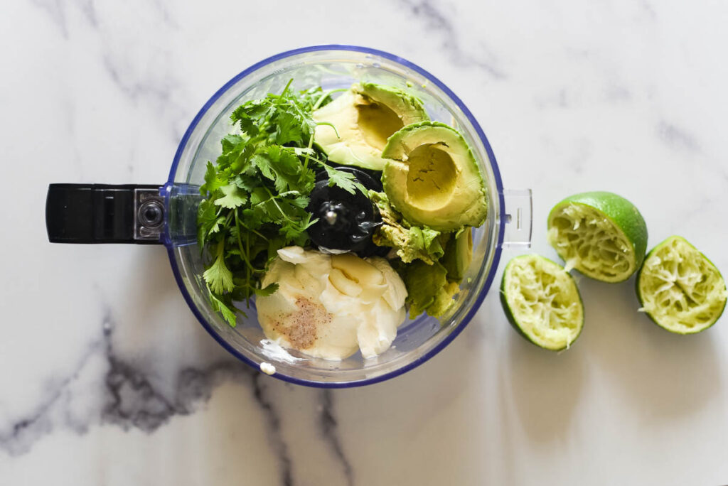 food processor cup with ingredients for avocado sauce