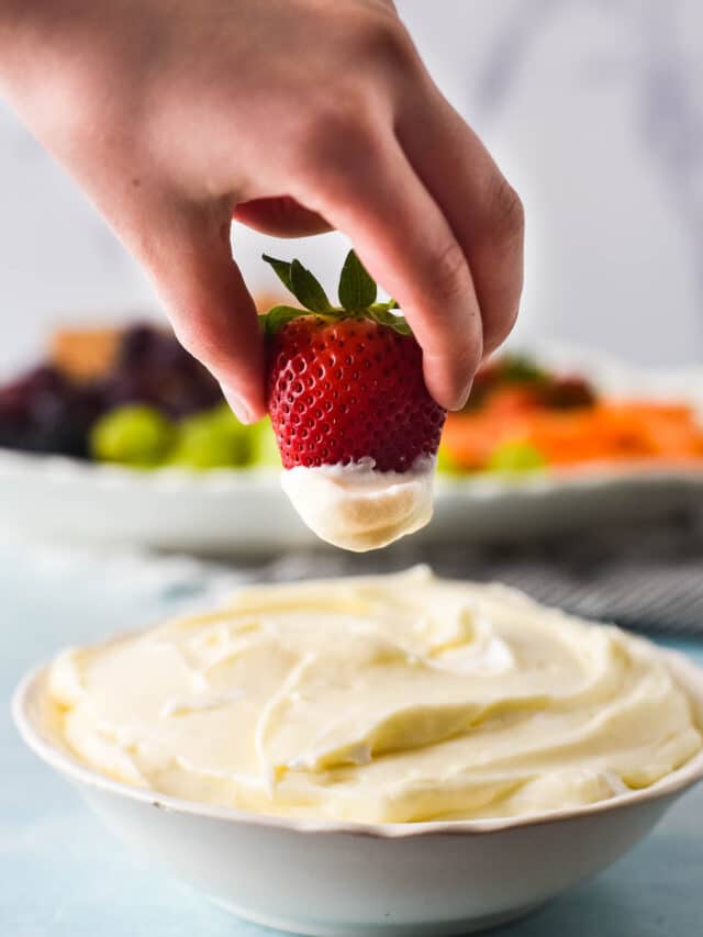 child hand dipping strawberry into marshmallow fluff