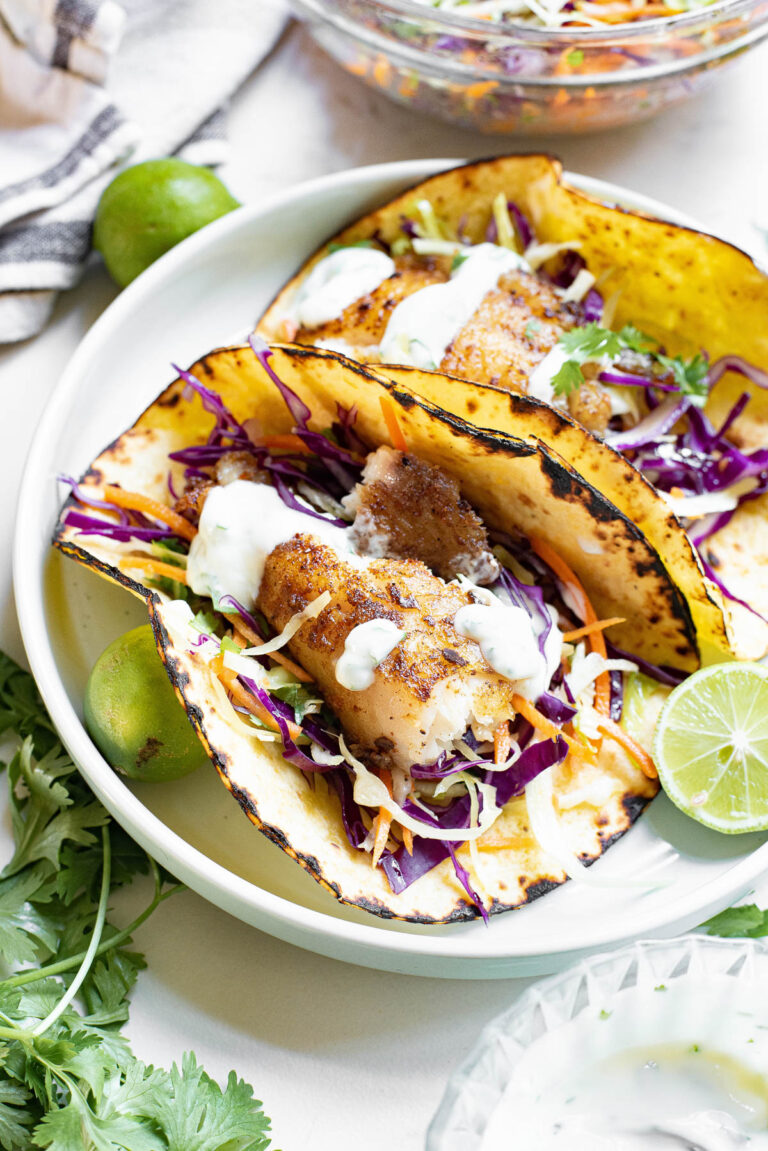 white plate with two tilapia tacos and toppings