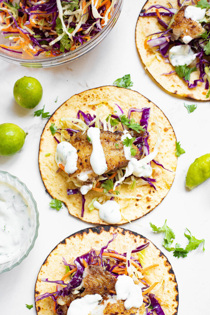 tortillas on table with tilapia, limes, and lime cilantro sauce