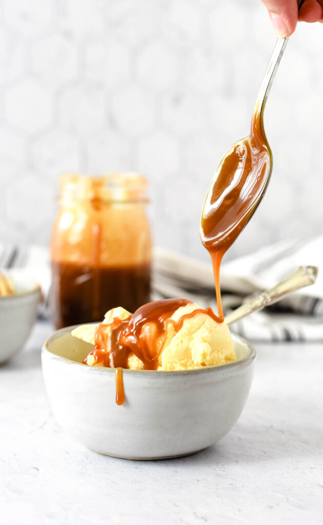 salted caramel sauce being drizzled from spoon onto bowl of ice cream
