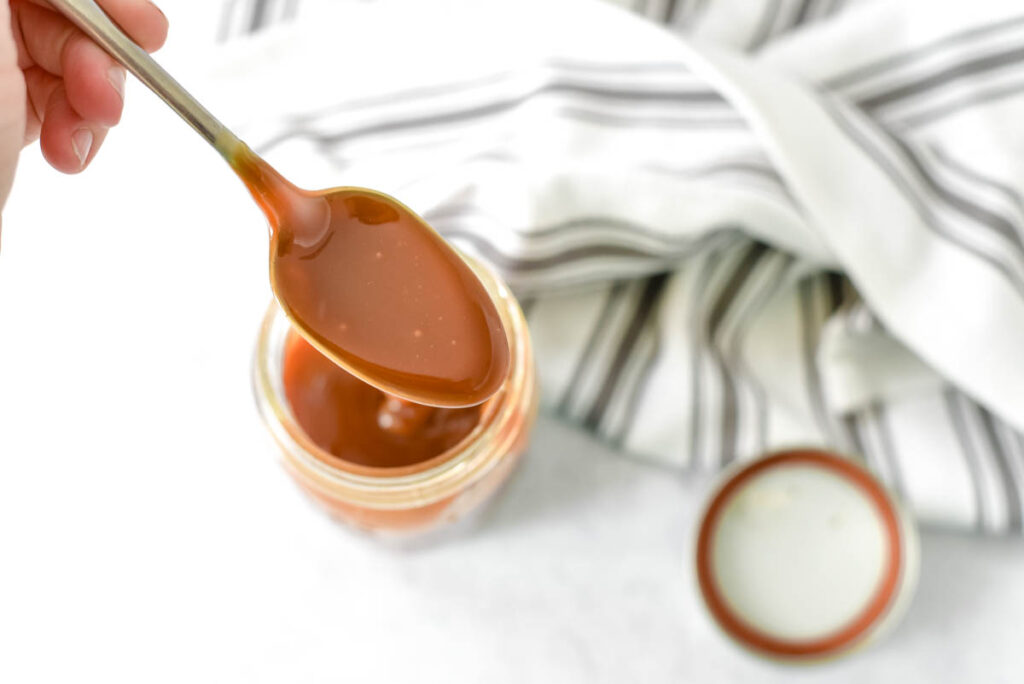spoon with caramel sauce over full mason jar