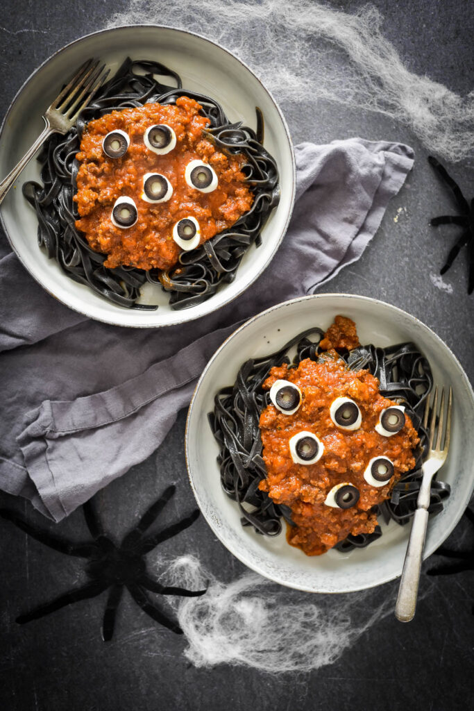 two bowls with black pasta, beef ragu and fake eyeballs