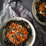 overhead image of halloween pasta in bowls with fake spiders and spiderwebs