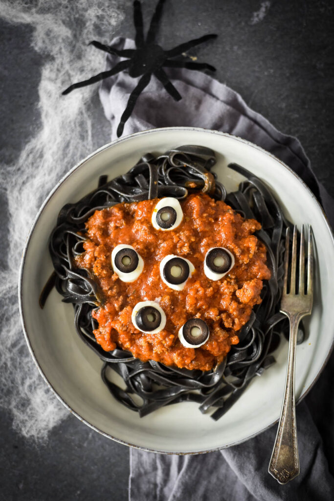 overhead view of bowl of halloween pasta with fake spider and spiderwebs