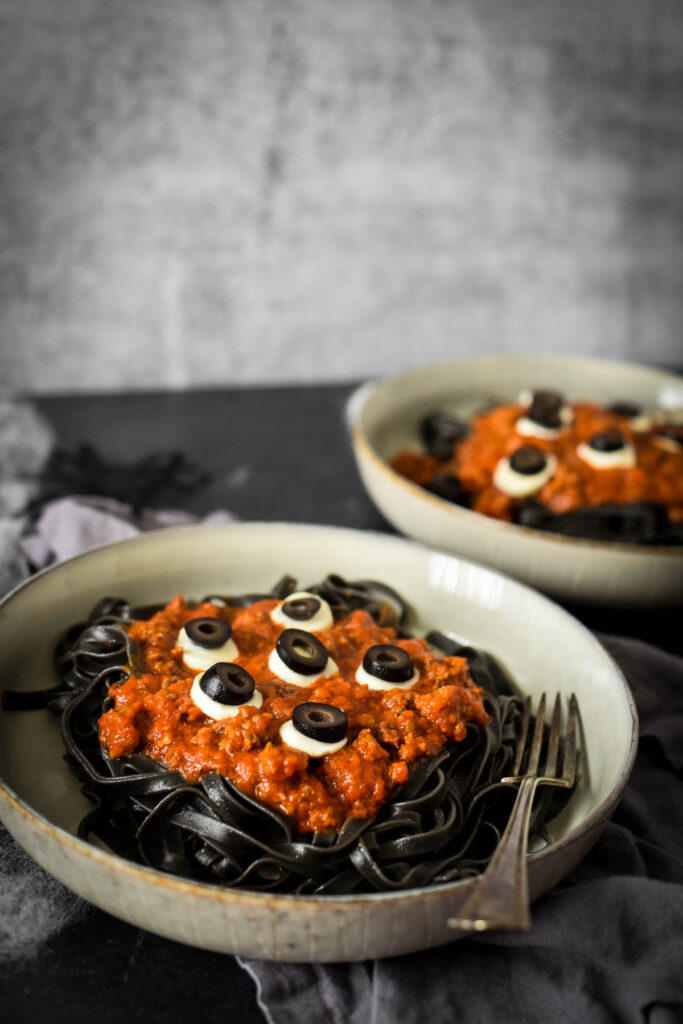 two bowls of squid ink pasta with ragu with olives as eyes