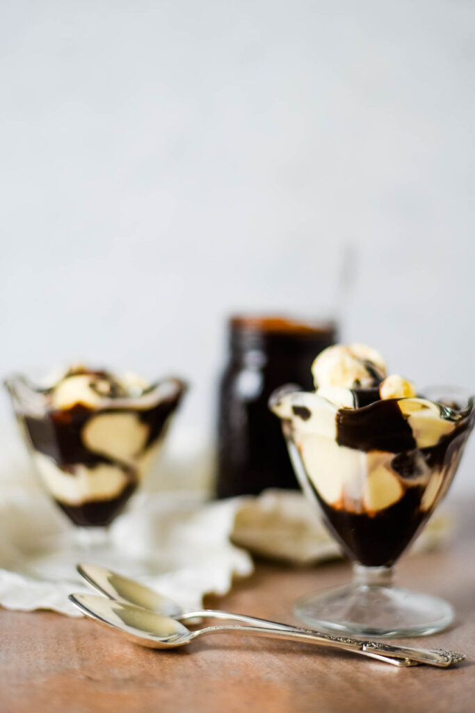 two glass dishes with vanilla ice cream and hot fudge sauce
