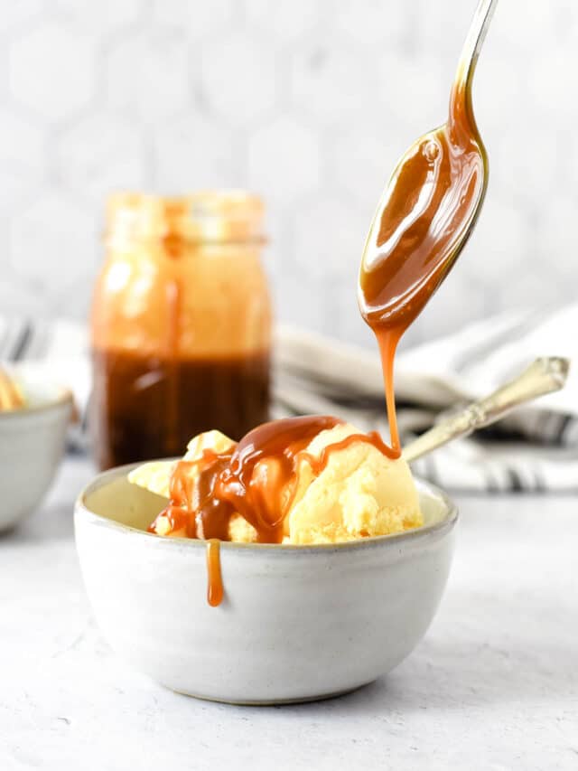 salted caramel sauce being drizzled from spoon onto bowl of ice cream