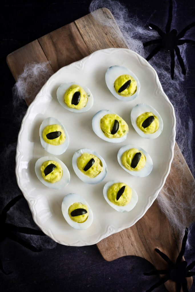 overhead view of white platter with deviled eggs with olive strips to look like eyeballs
