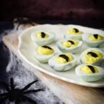 deviled eggs that look like eyeballs on white platter surrounded by cobwebs and fake spider