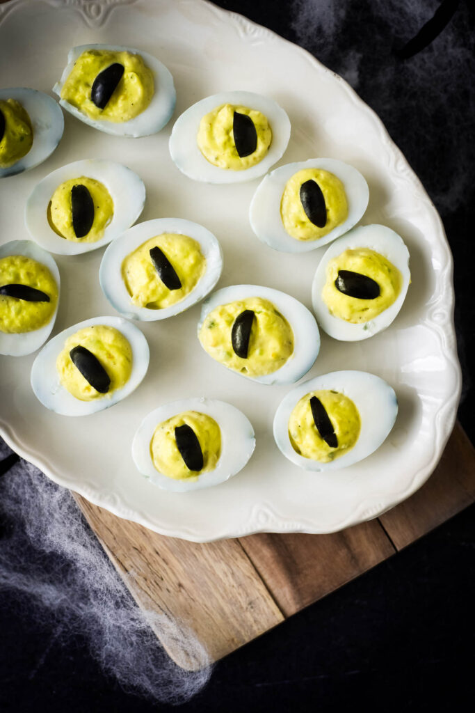 halloween deviled eggs on white platter surrounded by fake cobwebs