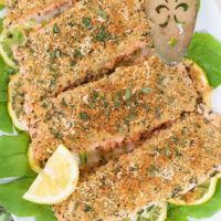Slices of herb crusted salmon on platter with lettuce and lemon slices