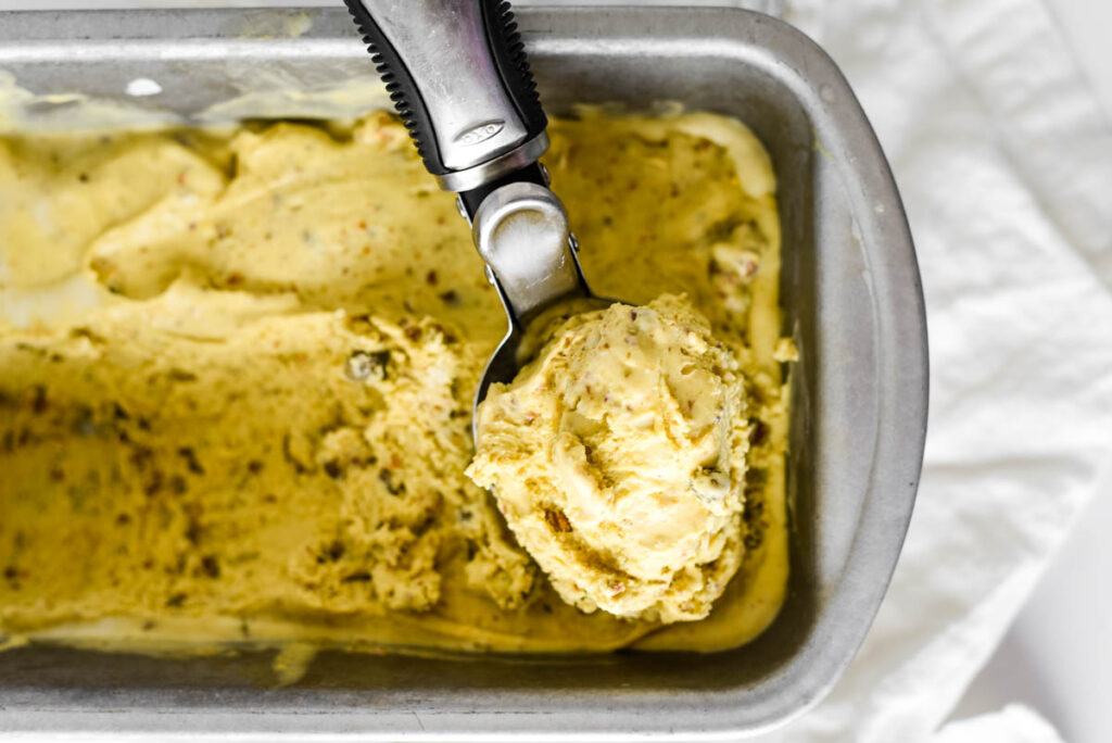 homemade pistachio ice cream in loaf pan with ice cream scoop on top