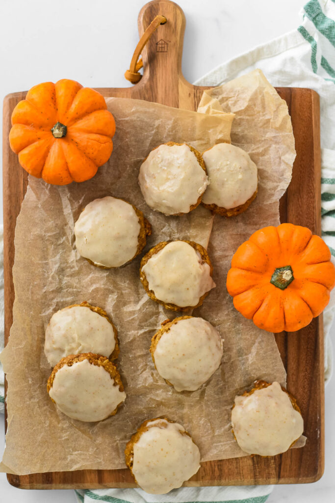 pumpkin cookies with brown butter glaze arranged on wooden cutting board with mini pumpkins
