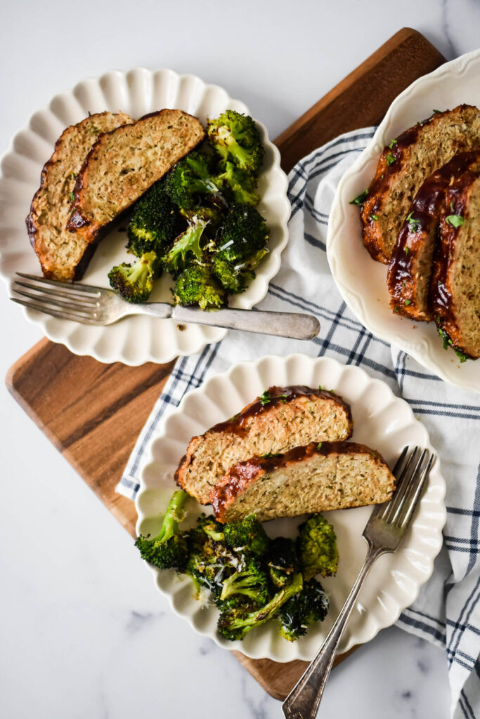 two white plates with chicken meatloaf and broccoli with forks beside