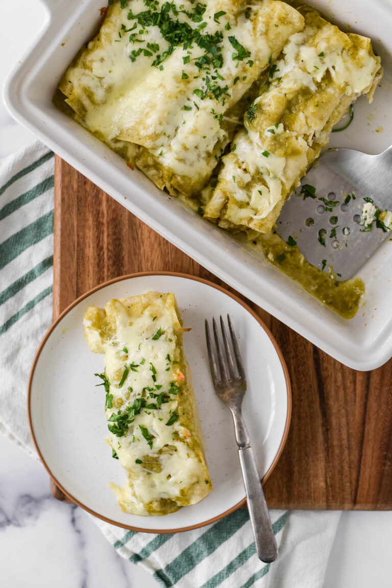 plate with two chicken enchiladas with green chile sauce on plate next to baking dish filled with more enchiladas