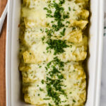 overhead view of white baking pan filled with enchiladas with chili sauce and white cheese topped with chopped cilantro