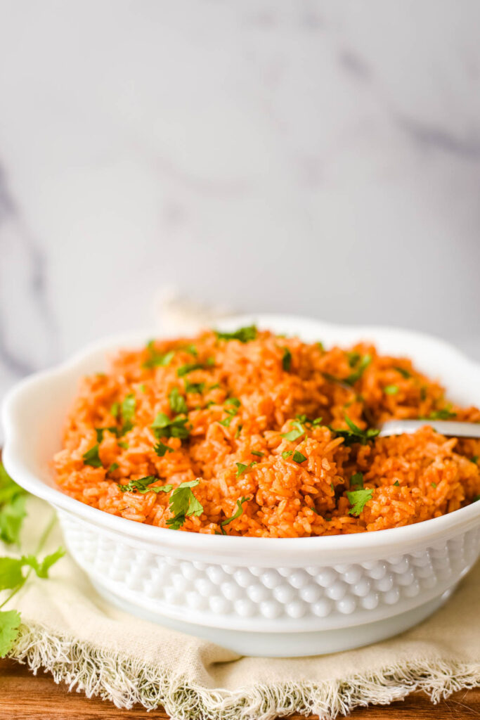 Spanish rice in white bowl with serving spoon and cloth napkin
