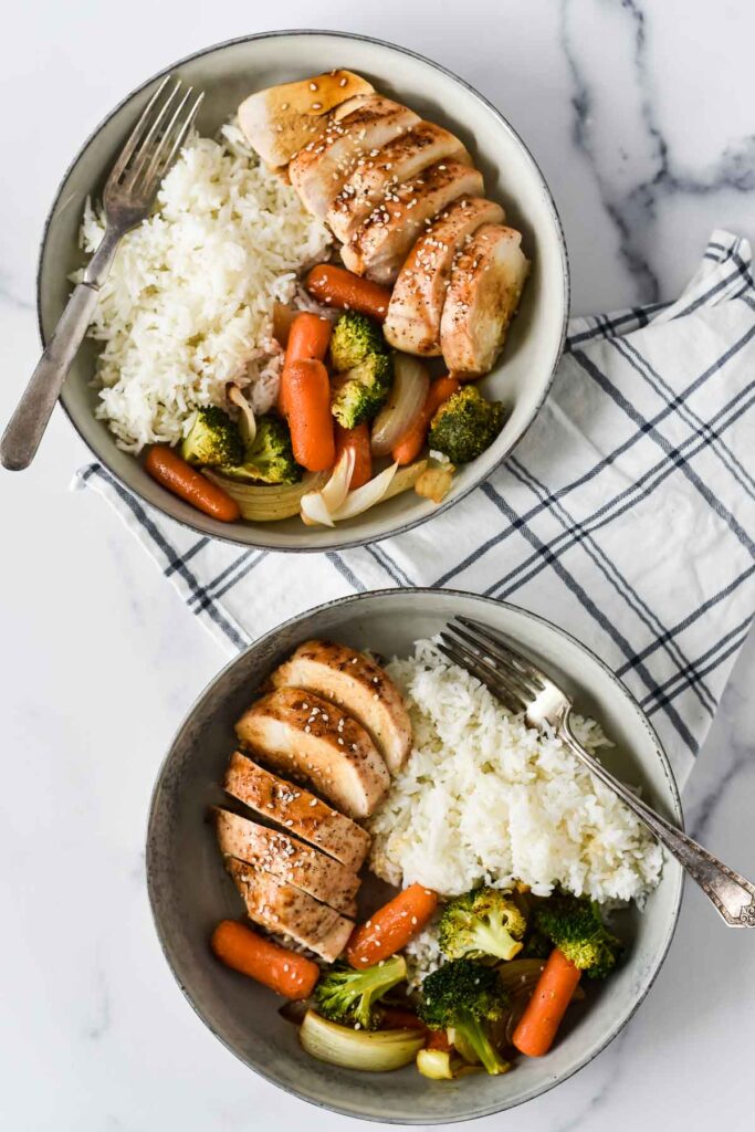 overhead view of two bowls of chicken teriyaki with rice, broccoli and carrots
