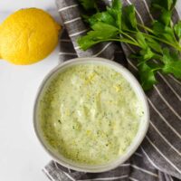 overhead view of small grey bowl with green sauce surrounded by lemon and fresh parsley