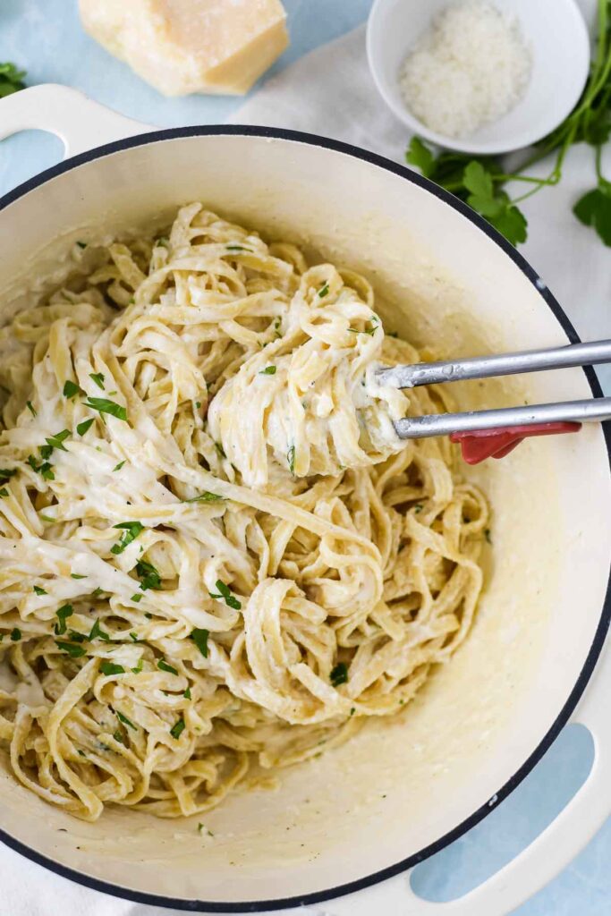 big pot filled with fettucine alfredo with kitchen tongs filled with pasta