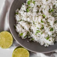 white rice in grey bowl with cilantro leaves on top and lime wedges beside