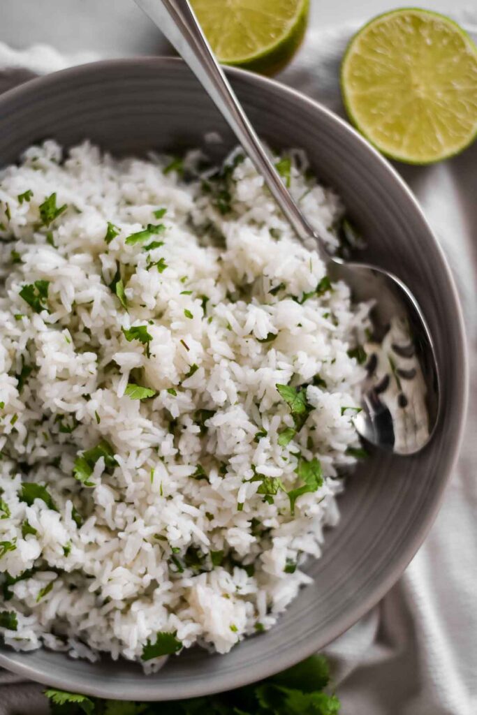 closeup of rice in a dish with cilantro leaves and lime wedges beside