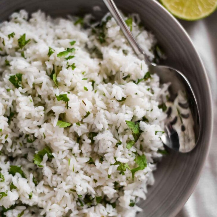 closeup of rice in a dish with cilantro leaves and lime wedges beside