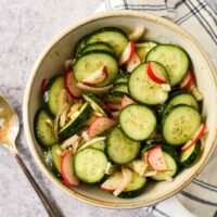 serving bowl filled with cucumber salad wtih serving spoon beside