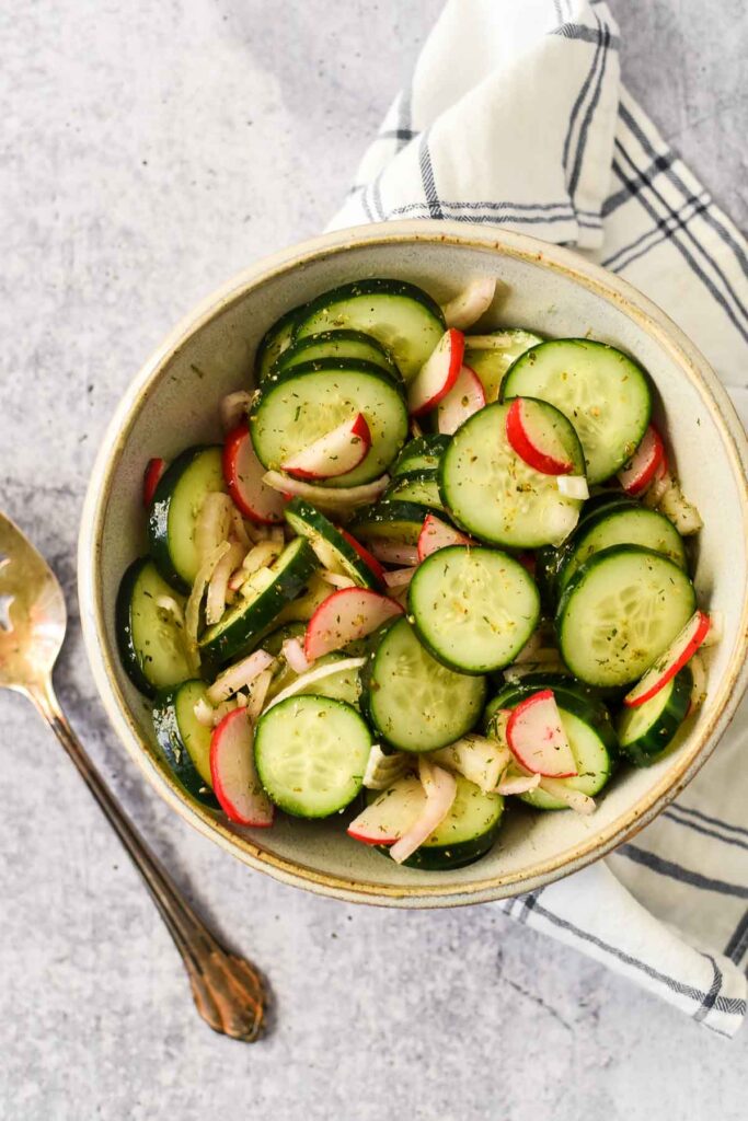 serving bowl filled with cucumber salad wtih serving spoon beside
