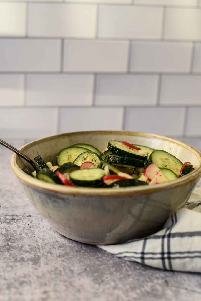 cucumbers and radishes in bowl with kitchen cloth on counter and tile behind