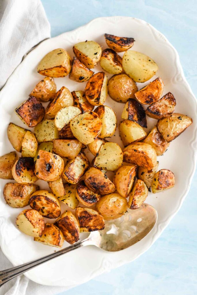 roasted potatoes on whit serving platter with spoon