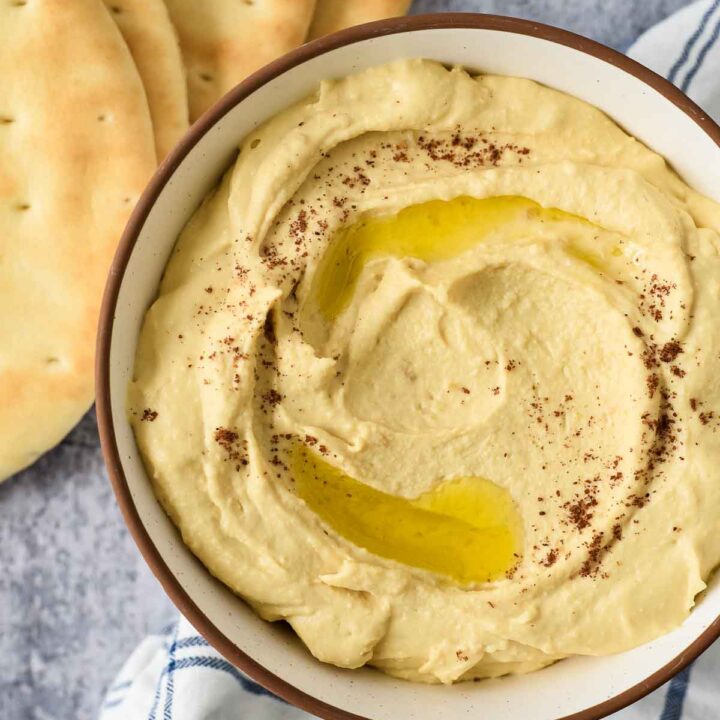 top-down view of bowl of hummus with olive oil drizzled on top and pita bread beside
