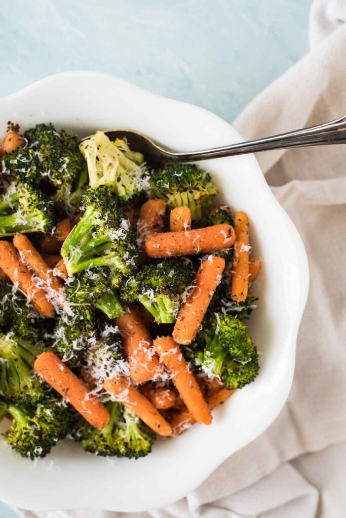 broccoli and carrots in a white serving bowl with parmesan sprinkled on top