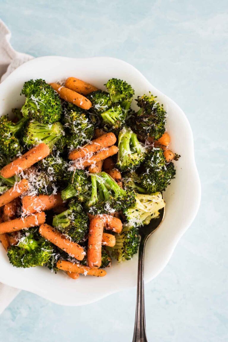 up close view of seasoning broccoli and carrots in serving bowl with spoon