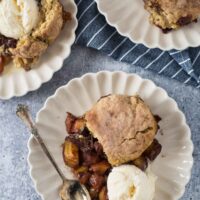 three white plates with peach cobbler made with sourdough biscuits
