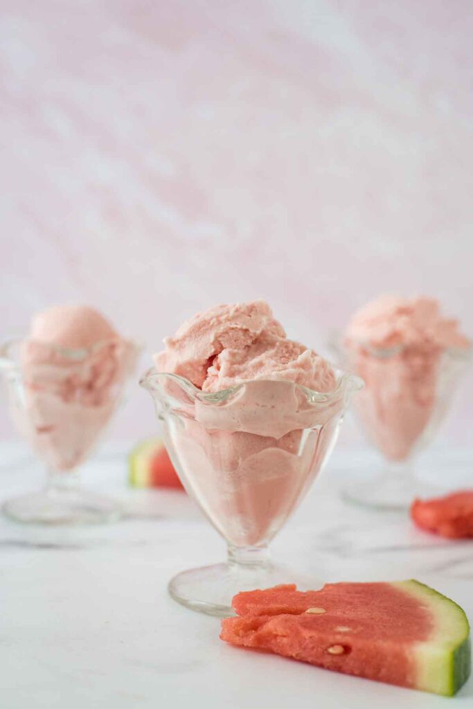 watermelon whip scooped in three fluted glass bowls with watermelon slices beside