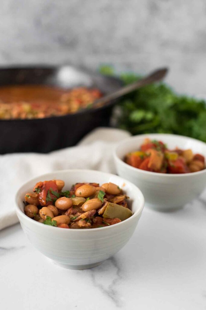 two small bowls of charro beans in front of cast iron skillet
