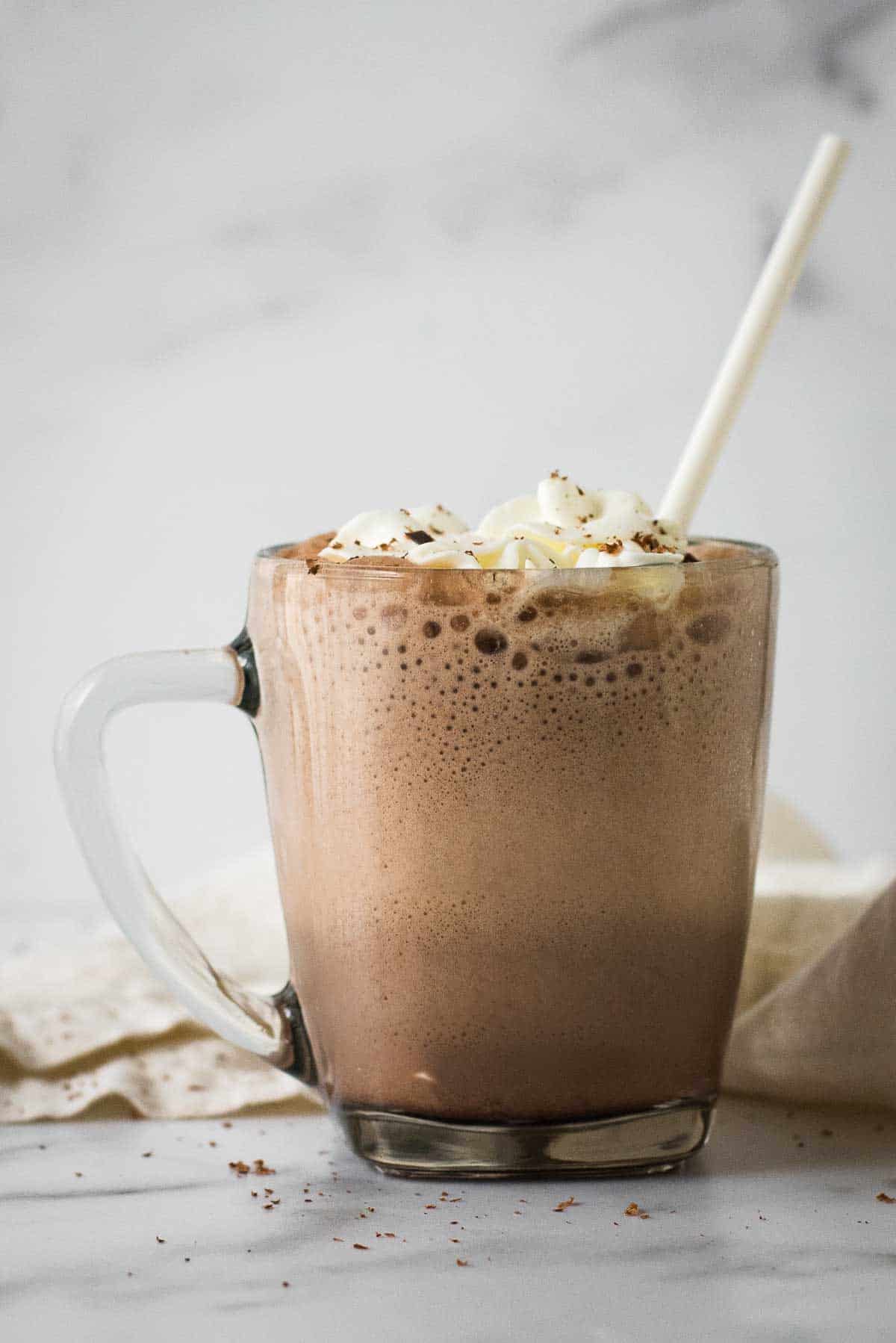 close up image of frozen hot chocolate in glass mug, topped with whipped cream and white paper straw