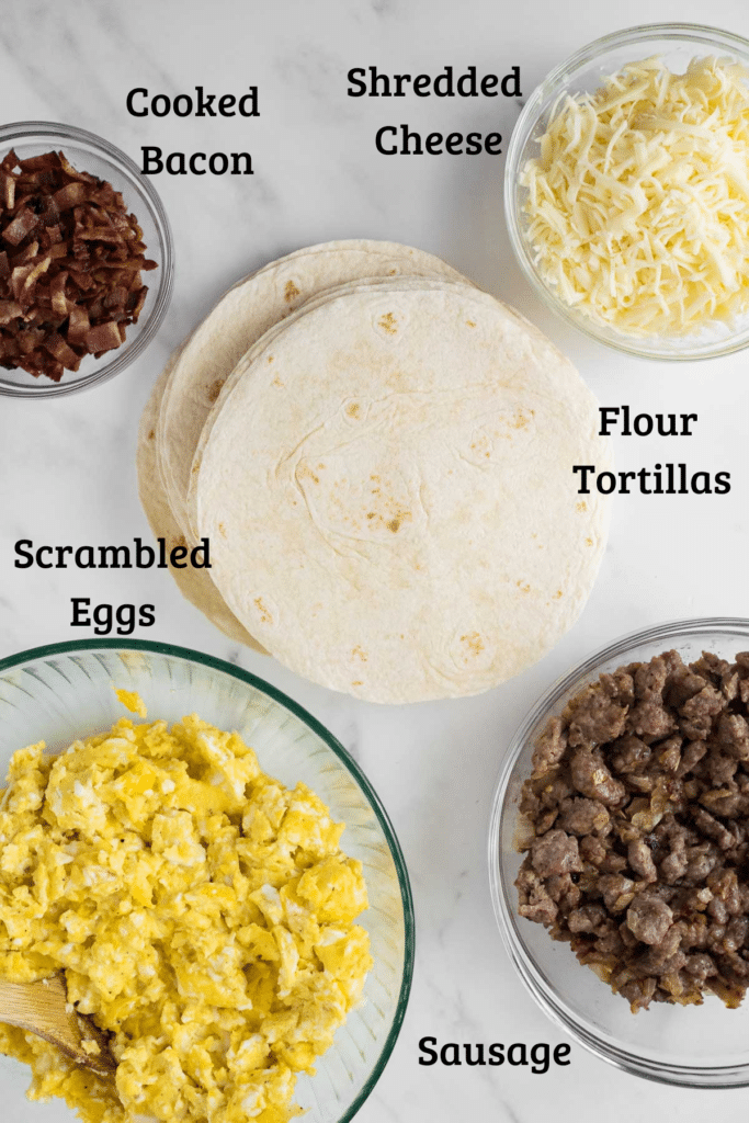bowls with scrambled eggs, sausage, bacon, and shredded cheese next to pile of tortillas