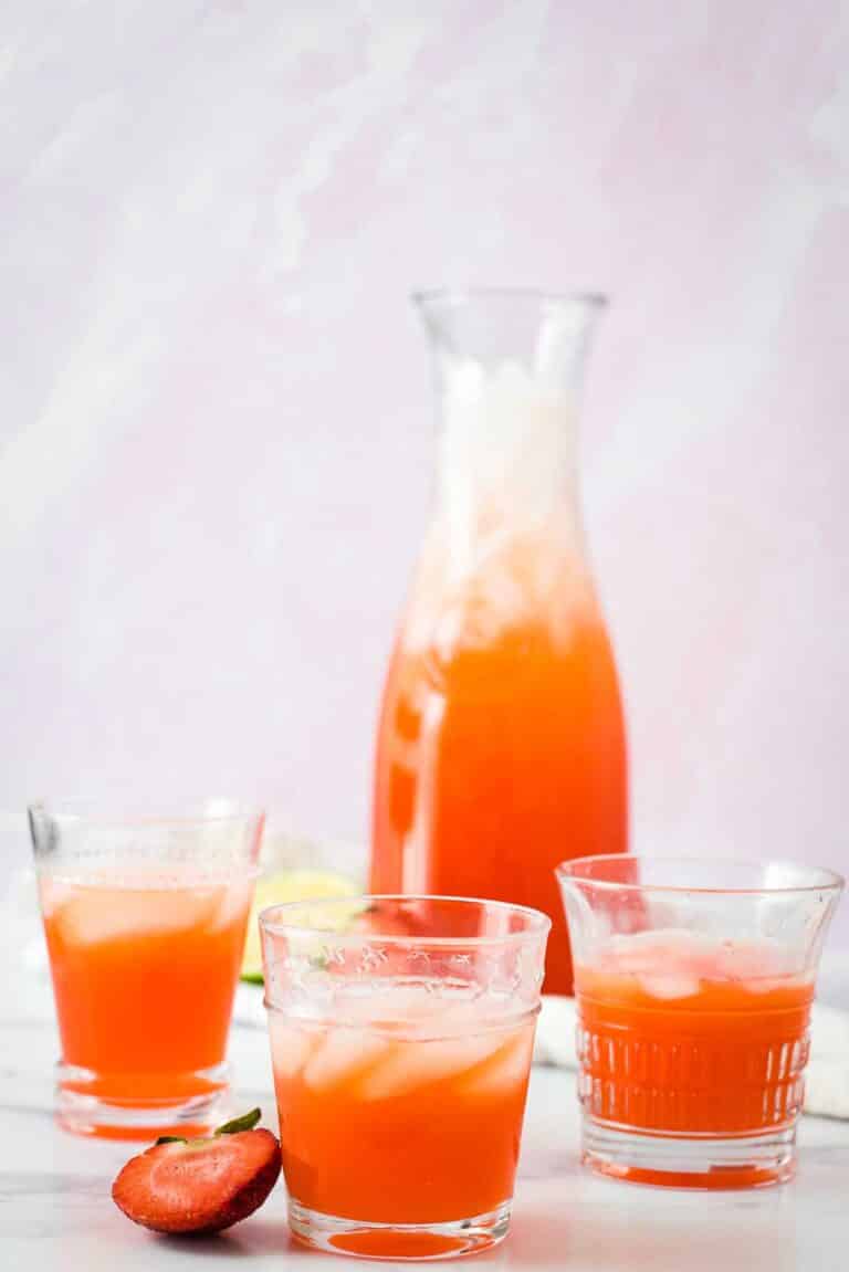three glasses of strawberry limeade and ice in front of filled pitcher
