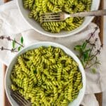 two white bowls of pasta with thai basil pesto and forks, thai basil flowers around bowls