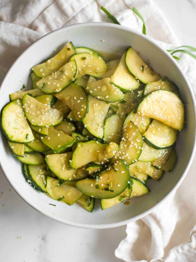 white bowl with sautéed zucchini cut into half moon shapes, sprinkled with sesame seeds and green onions