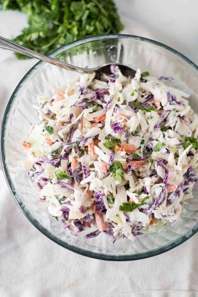 cilantro lime slaw in glass bowl with serving spoon