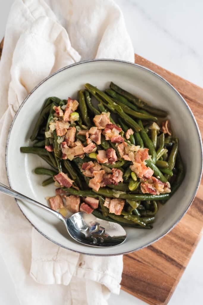 overhead view of green beans and bacon in grey bowl with serving spoon